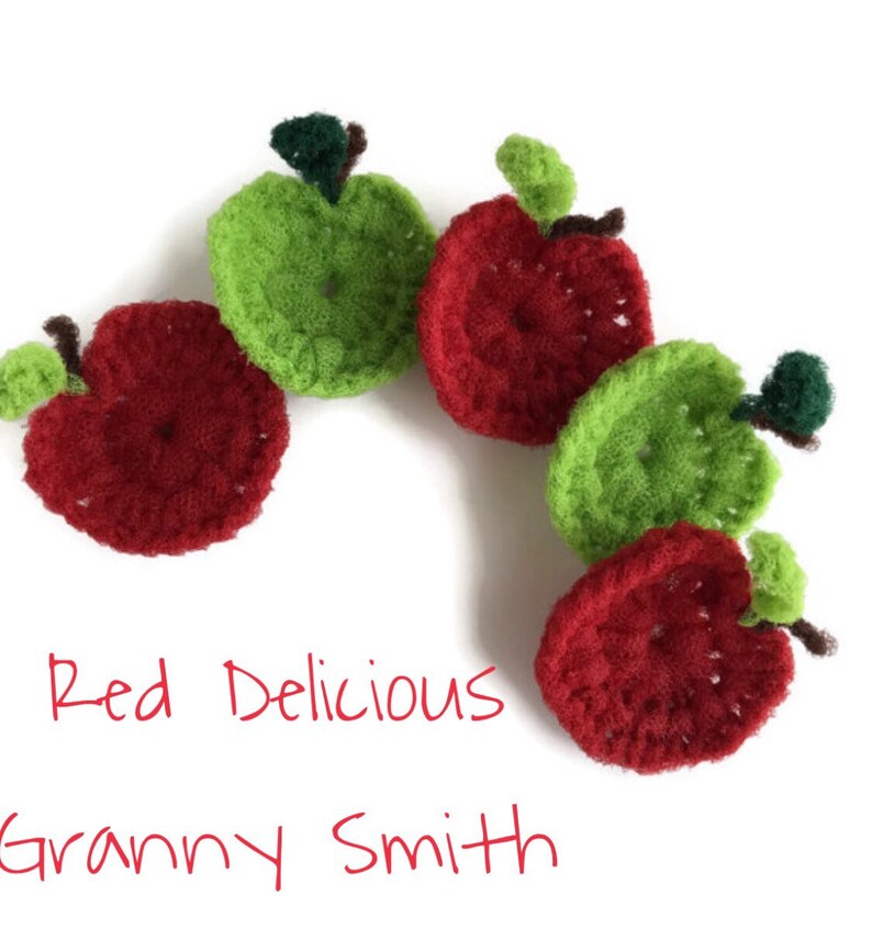 Puede incluir: Manzanas de crochet en rojo y verde, dispuestas en semic&iacute;rculo. El texto "Red Delicious Granny Smith" est&aacute; escrito debajo de las manzanas.