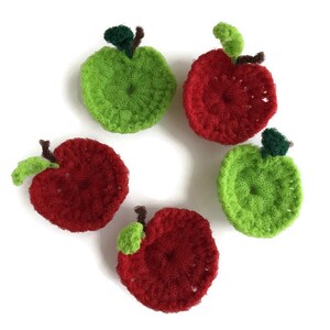 Puede incluir: Cinco pa&ntilde;os de cocina de ganchillo con forma de manzana, dos rojos y tres verdes, dispuestos en c&iacute;rculo sobre un fondo blanco.
