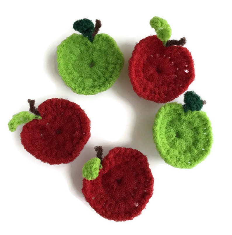 Puede incluir: Cinco pa&ntilde;os de cocina de ganchillo con forma de manzana, dos rojos y tres verdes, dispuestos en c&iacute;rculo sobre un fondo blanco.