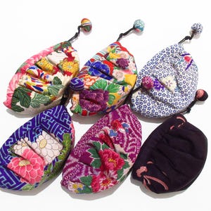 May include: Six small, gathered fabric pouches with drawstring closures topped with decorative beads. Five pouches feature vibrant, multi-colored floral and geometric patterns, while one pouch is solid dark purple with a subtle pink trim.
