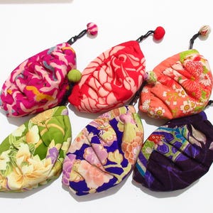 May include: Six small, fabric pouches with gathered, rounded shapes and zipper closures. Each pouch features a distinct, colorful floral or patterned textile design in shades of pink, red, orange, green, blue, and purple, finished with a small fabric ball.