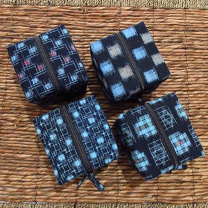 May include: Four square fabric pouches with dark blue and black backgrounds, each featuring a central zipper closure. The pouches display various geometric patterns in shades of light blue, white, and subtle red, arranged in grid-like or block designs.