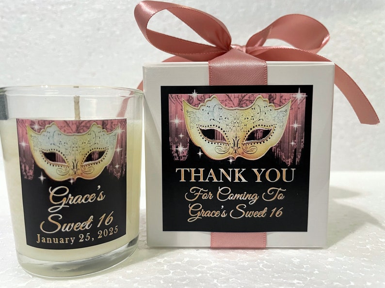 Op de afbeelding: Een witte kaars in een glazen pot met een zwart en roze etiket met de tekst "Grace's Sweet 16 January 25, 2025". Het etiket heeft ook een gouden en witte maskerade masker. De kaars is verpakt in een witte doos met een roze lint en een zwart en roze etiket met de tekst "Bedankt voor je komst naar Grace's Sweet 16".
