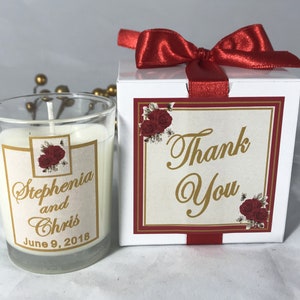 May include: A white box with a red bow and a red and gold label that says "Thank You". The box contains a small glass jar candle with a white label that says "Stephania and Chris June 9, 2018".