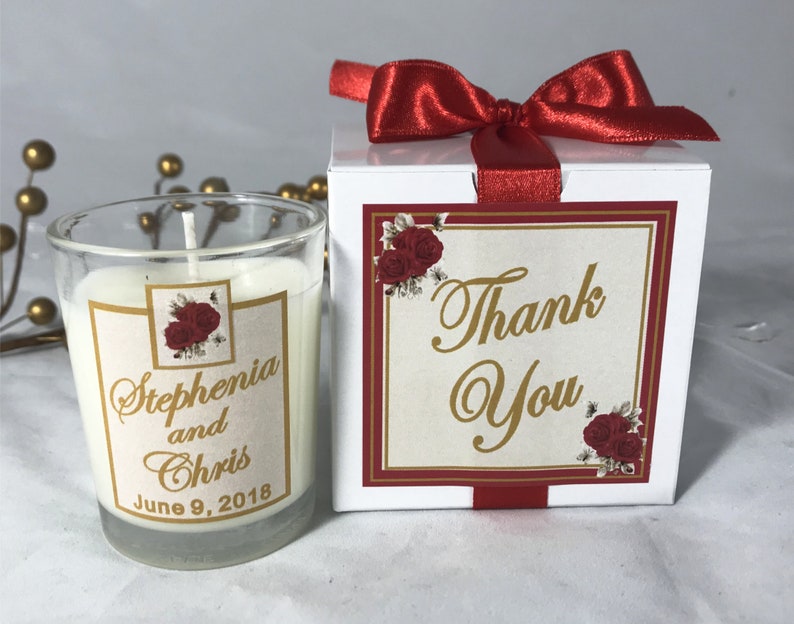 May include: A white box with a red bow and a red and gold label that says "Thank You". The box contains a small glass jar candle with a white label that says "Stephania and Chris June 9, 2018".