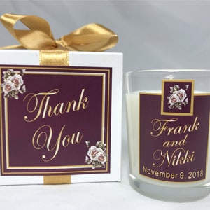 May include: A white box with a gold ribbon and a burgundy label that says "Thank You" in gold lettering. The box contains a small glass jar candle with a burgundy label that says "Frank and Nikki November 9, 2018" in gold lettering.