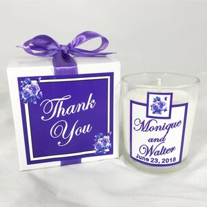 May include: A small white candle in a clear glass jar with a purple and white label that says "Monique and Walter June 23, 2018". The candle is in a white box with a purple ribbon and a purple and white label that says "Thank You".