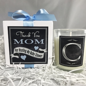 May include: A white gift box with a blue ribbon tied around it. The box has a black and white label that says "Thank You MOM For Hosting My Baby Shower".  A small glass candle jar with a black and white label with a silver letter "C" on it.