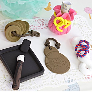 May include: A set of five traditional Korean crafts made of clay. The set includes a money bag, a brush and inkwell, a coin charm, a horse charm, and a knotted rope charm.