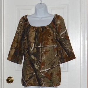 May include: A brown and green camouflage print top with a scoop neck and 3/4 sleeves.