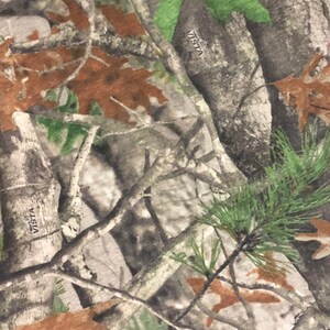 May include: Camouflage fabric with a brown, green, and gray pattern. The fabric has the word "VISTA" printed on it.