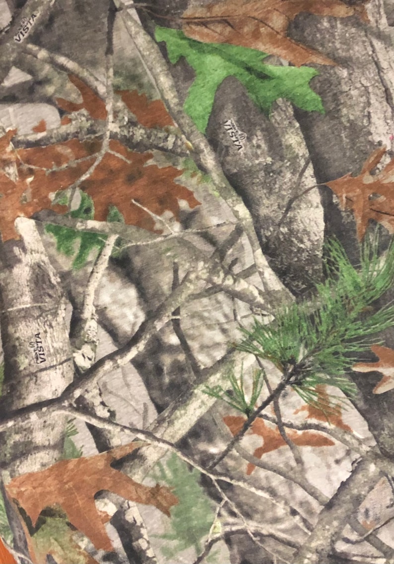 May include: Camouflage fabric with a brown, green, and gray pattern. The fabric has the word "VISTA" printed on it.