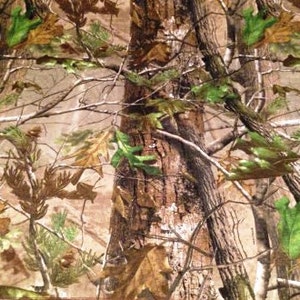 May include: Camouflage fabric with a brown, green, and tan pattern featuring tree trunks, branches, and leaves.