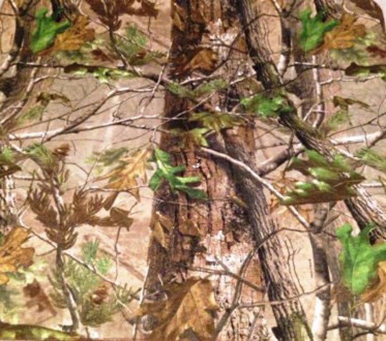 May include: Camouflage fabric with a brown, green, and tan pattern featuring tree trunks, branches, and leaves.