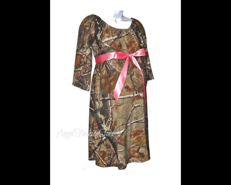 May include: A camouflage maternity dress with a pink ribbon tied around the waist. The dress has a scoop neckline and 3/4 sleeves.