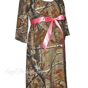 May include: A camouflage print maternity dress with a pink satin ribbon tied at the waist. The dress has a scoop neckline and 3/4 sleeves.
