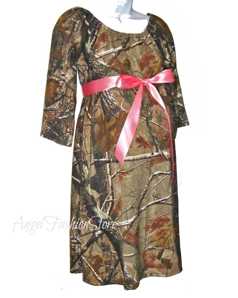 May include: A camouflage print maternity dress with a pink satin ribbon tied at the waist. The dress has a scoop neckline and 3/4 sleeves.