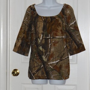 May include: A brown, green, and white camouflage print top with a scoop neck and 3/4 sleeves.