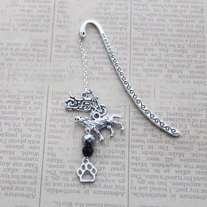 May include: Silver bookmark with a chain and charms, including a motorcycle, a wolf, a paw print, and black beads. The bookmark is on a page of a book with text about travel and adventure.