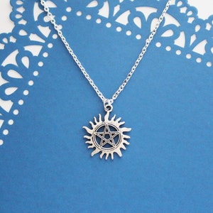 K&ouml;nnte beinhalten: Eine silberne Halskette mit einem Pentagramm-Anh&auml;nger in einem Sonnensymbol. Die Kette liegt auf einem blauen Hintergrund mit einem Spitzenmuster.