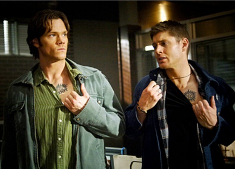 K&ouml;nnte beinhalten: Zwei M&auml;nner in blauen Jeansjacken, einer mit einem gr&uuml;n gestreiften Hemd und der andere mit einem schwarzen Hemd, beide mit einem Tattoo eines Symbols auf der Brust.