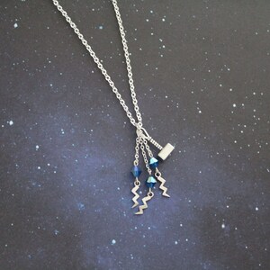 May include: A silver necklace with a small silver hammer charm and three dangling blue crystal beads with silver lightning bolt charms.