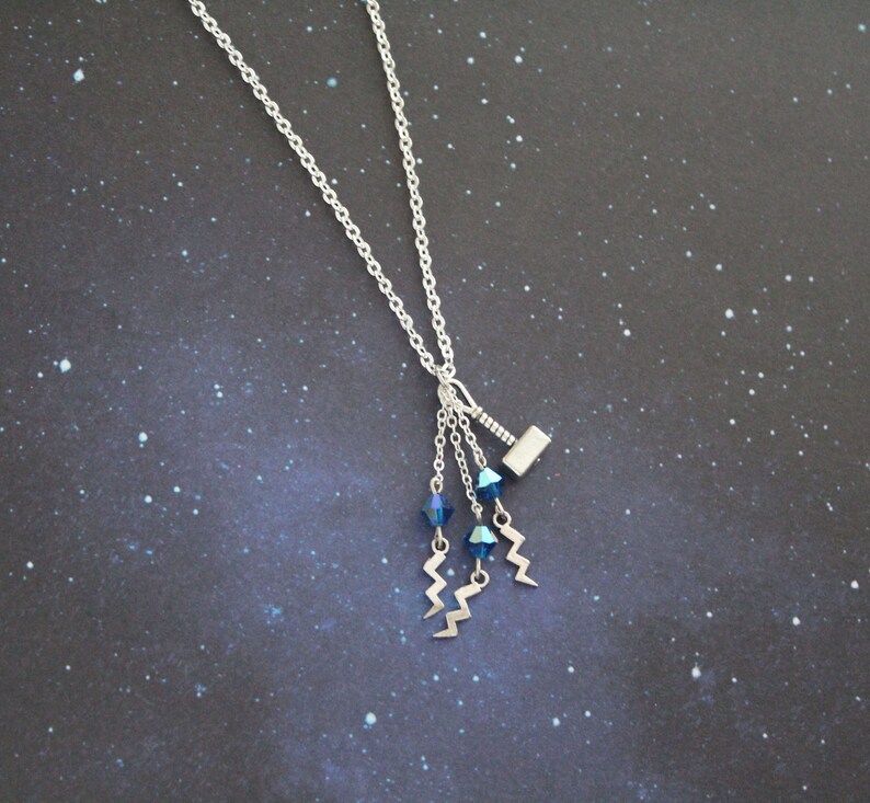 May include: A silver necklace with a small silver hammer charm and three dangling blue crystal beads with silver lightning bolt charms.