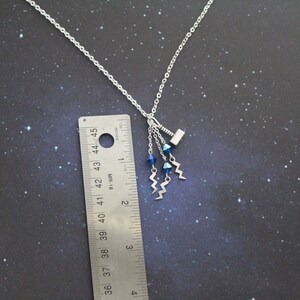 May include: A silver necklace with a small silver hammer charm and three blue crystal beads hanging from it. The necklace is about 18 inches long.