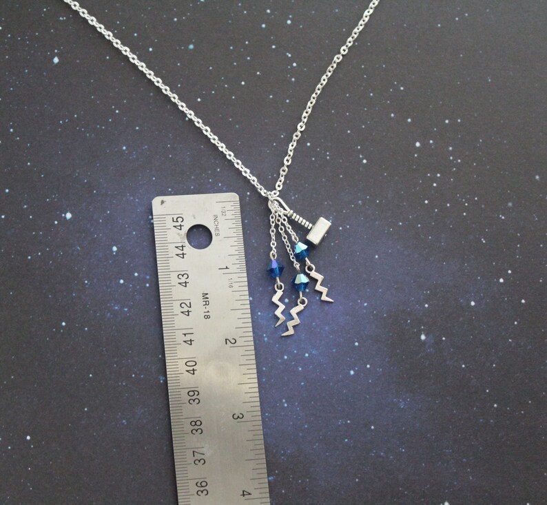 May include: A silver necklace with a small silver hammer charm and three blue crystal beads hanging from it. The necklace is about 18 inches long.