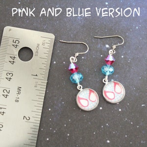 Puede incluir: Pendientes rosas y azules con un dise&ntilde;o de m&aacute;scara de Spiderman. Cada pendiente tiene un gancho plateado, con cuentas de cristal rosas y azules. La m&aacute;scara de Spiderman est&aacute; en un bisel plateado. El texto "PINK AND BLUE VERSION" est&aacute; en la parte superior.