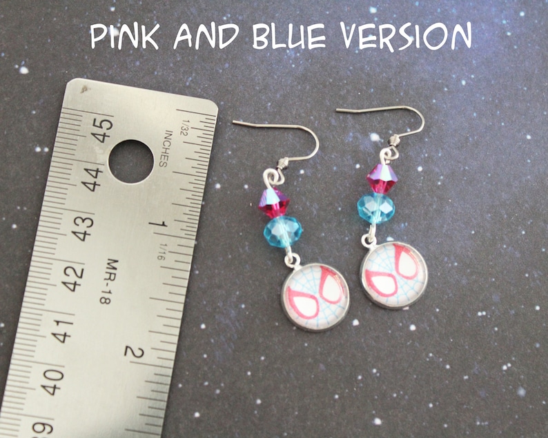 Puede incluir: Pendientes rosas y azules con un dise&ntilde;o de m&aacute;scara de Spiderman. Cada pendiente tiene un gancho plateado, con cuentas de cristal rosas y azules. La m&aacute;scara de Spiderman est&aacute; en un bisel plateado. El texto "PINK AND BLUE VERSION" est&aacute; en la parte superior.