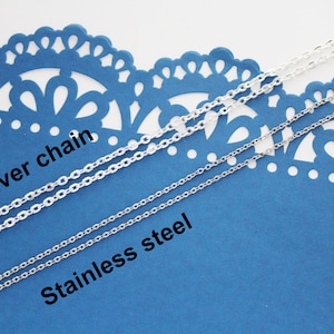 K&ouml;nnte beinhalten: Zwei silberne Ketten auf blauem Hintergrund. Die obere Kette ist mit "Silberkette" und die untere Kette mit "Edelstahl" beschriftet.