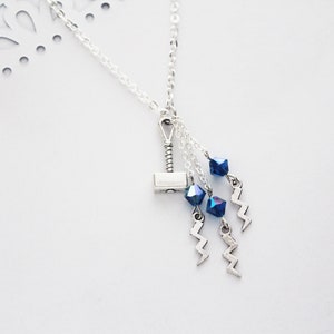 May include: A silver necklace with a silver hammer charm and blue crystal beads. The necklace also has silver lightning bolt charms.