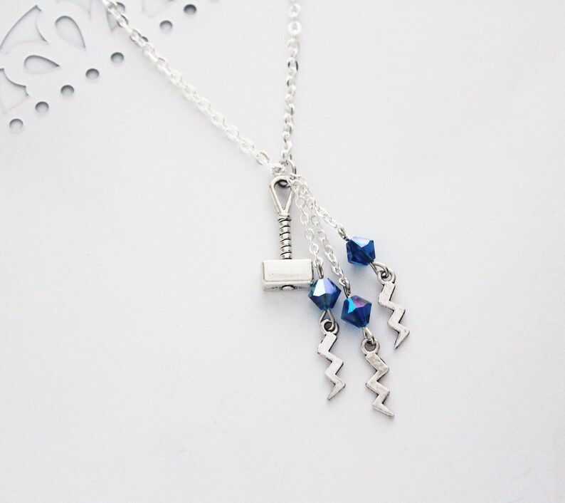 May include: A silver necklace with a silver hammer charm and blue crystal beads. The necklace also has silver lightning bolt charms.