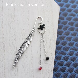Puede incluir: Marcap&aacute;ginas de pluma de plata con un dije de p&aacute;jaro negro y cuentas de cristal negras y rojas colgantes. "Versi&oacute;n con dije negro" est&aacute; escrito en el fondo.