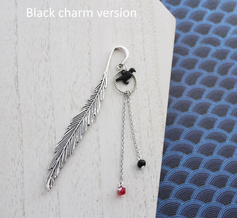 Puede incluir: Marcap&aacute;ginas de pluma de plata con un dije de p&aacute;jaro negro y cuentas de cristal negras y rojas colgantes. "Versi&oacute;n con dije negro" est&aacute; escrito en el fondo.