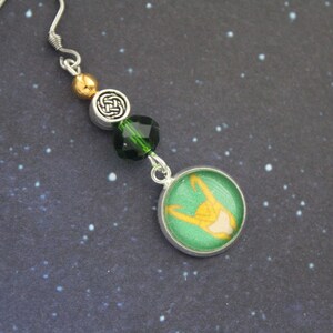 以下が含まれることがあります： 緑と金のデザインのシルバーカラーのドロップイヤリング。イヤリングは、黄色のフィギュア、緑と金のビーズ、ケルトノットチャームを備えた緑と金の円形チャームが特徴です。