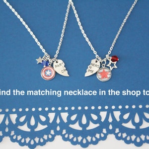 K&ouml;nnte beinhalten: Zwei silberne Halsketten mit Anh&auml;ngern. Eine hat einen Captain America Schild-Anh&auml;nger und einen gebrochenen Herz-Anh&auml;nger mit der Aufschrift "PART CR". Die andere hat einen Stern-Anh&auml;nger und einen gebrochenen Herz-Anh&auml;nger mit der Aufschrift "NERS N IME". Beide haben Stern- und Perlenakzente.