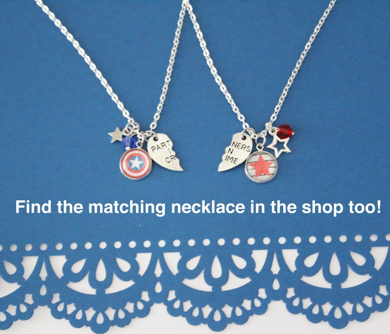 K&ouml;nnte beinhalten: Zwei silberne Halsketten mit Anh&auml;ngern. Eine hat einen Captain America Schild-Anh&auml;nger und einen gebrochenen Herz-Anh&auml;nger mit der Aufschrift "PART CR". Die andere hat einen Stern-Anh&auml;nger und einen gebrochenen Herz-Anh&auml;nger mit der Aufschrift "NERS N IME". Beide haben Stern- und Perlenakzente.