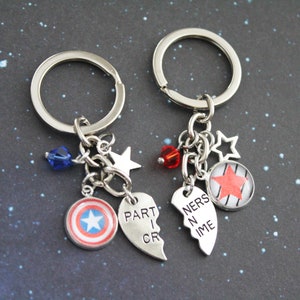 K&ouml;nnte beinhalten: Zwei passende Schl&uuml;sselanh&auml;nger mit silbernen Ringen und Anh&auml;ngern. Einer hat einen Captain America Schild-Anh&auml;nger, eine blaue Kristallperle und einen Stern-Anh&auml;nger. Der andere hat einen roten Stern-Anh&auml;nger, eine rote Kristallperle und einen Stern-Anh&auml;nger. Die Anh&auml;nger lesen "PART I CR" und "NERS N IME".