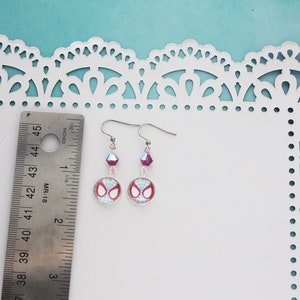 Puede incluir: Pendientes plateados de Spider-Man con un dise&ntilde;o rojo y blanco. Cada pendiente presenta un dije redondo con el logotipo de Spider-Man, una cuenta de cristal p&uacute;rpura y un gancho. Los pendientes miden aproximadamente 2.5 cm de largo.