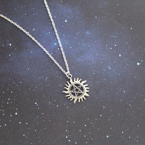 K&ouml;nnte beinhalten: Eine silberne Halskette mit einem Pentagramm-Anh&auml;nger in Form einer Sonne. Der Anh&auml;nger ist detailliert und hat ein schwarzes Pentagramm im Inneren.