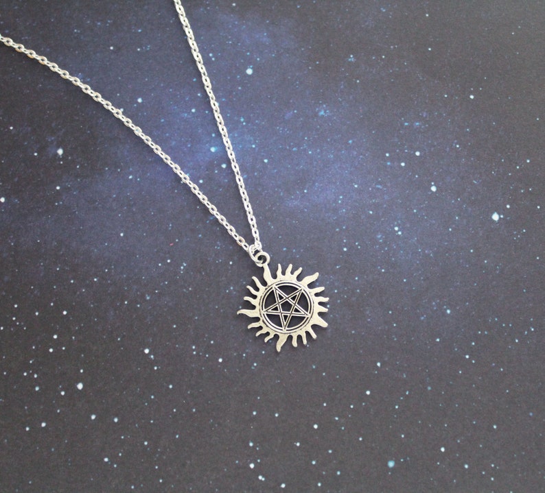 K&ouml;nnte beinhalten: Eine silberne Halskette mit einem Pentagramm-Anh&auml;nger in Form einer Sonne. Der Anh&auml;nger ist detailliert und hat ein schwarzes Pentagramm im Inneren.