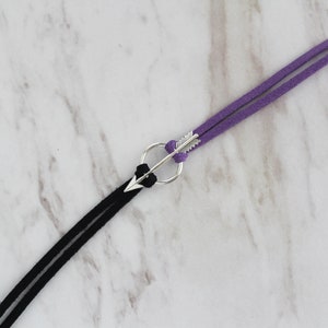 May include: A black and purple suede cord bracelet with a silver arrow charm.