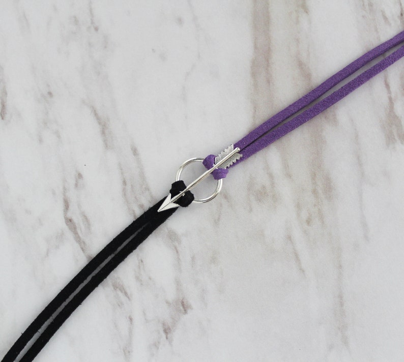 May include: A black and purple suede cord bracelet with a silver arrow charm.