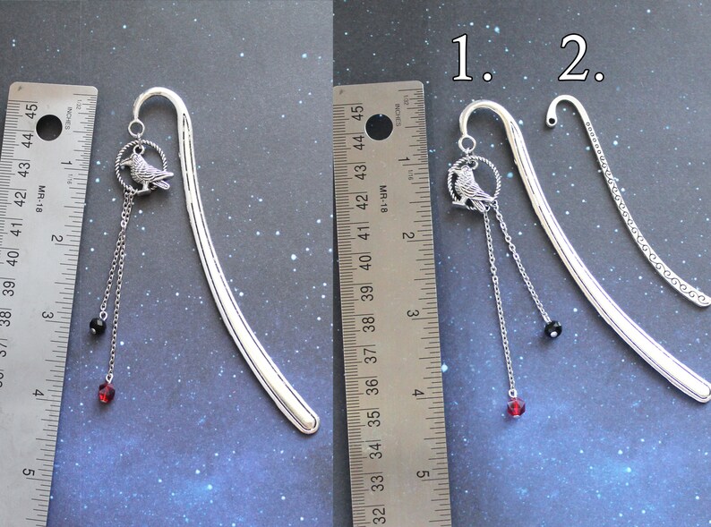 Puede incluir: Dos dise&ntilde;os de marcap&aacute;ginas de plata con un dije de p&aacute;jaro y cuentas colgantes. El marcap&aacute;ginas de la izquierda tiene una cuenta negra y una cuenta roja. El marcap&aacute;ginas de la derecha tiene una cuenta negra y una cuenta roja. Los marcap&aacute;ginas se miden con una regla.
