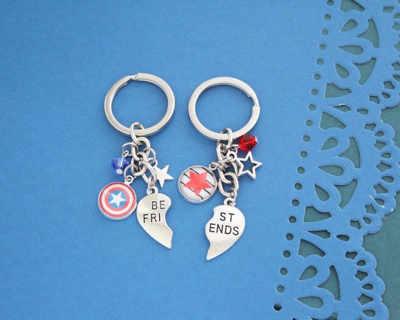 K&ouml;nnte beinhalten: Zwei passende Schl&uuml;sselanh&auml;nger mit silbernen Ringen und Anh&auml;ngern. Einer hat einen Schildanh&auml;nger und die Worte "BE FRI" auf einem herzf&ouml;rmigen Anh&auml;nger. Der andere hat einen Sternanh&auml;nger und die Worte "ST ENDS" auf einem herzf&ouml;rmigen Anh&auml;nger. Beide haben Stern- und Perlenakzente.