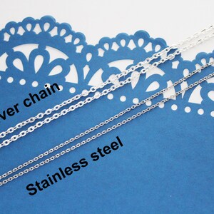 May include: Two silver chains on a blue background. The top chain is labelled "Silver chain" and the bottom chain is labelled "Stainless steel".