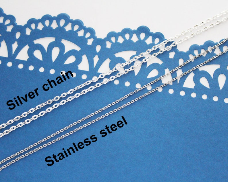 May include: Two silver chains on a blue background. The top chain is labelled "Silver chain" and the bottom chain is labelled "Stainless steel".