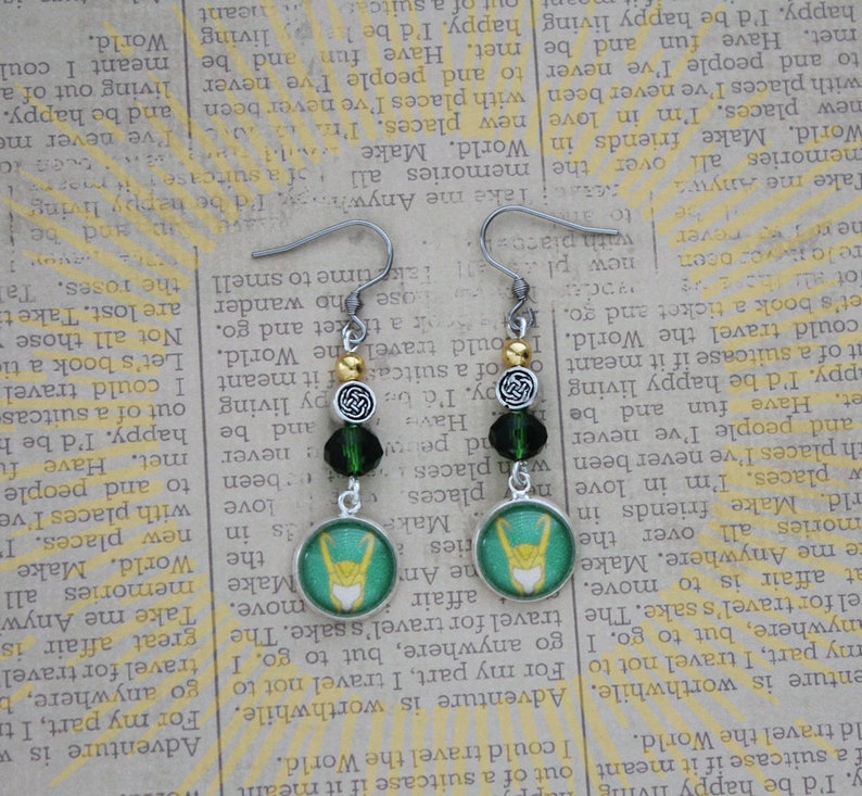 以下が含まれることがあります： 緑と白の円形デザインに様式化されたシンボルが特徴の、シルバーカラーのぶら下がりピアス。ピアスには濃い緑色のビーズと金色のビーズが付いています。ユニークなアクセサリー。